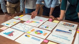 Financial and business documents on table with multiethnic hands working on it. Latin business manager with colleagues working on new startup project. Closeup business man and businesswoman hands understanding pie and bar graphs during meeting.