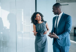 Shot of two young colleagues having a discussion in modern office. Confident young business people working together in the office. Corporate business persons discussing new project and sharing ideas in the workplace.